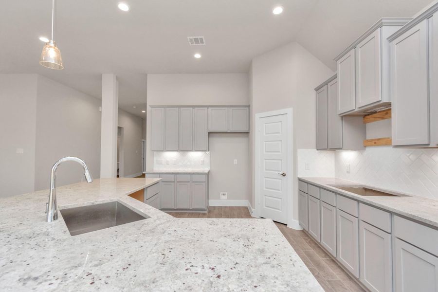 Culinary haven, featuring granite countertops, a tile backsplash, stainless steel appliances, 42” upper cabinets, and undercabinet lighting. Sample photo of completed home with similar floor plan. Actual colors and selections may vary. Culinary haven, featuring granite countertops, a tile backsplash, stainless steel appliances, 42” upper cabinets, and undercabinet lighting. Sample photo of completed home with similar floor plan. Actual colors and selections may vary.