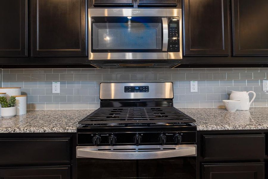 Kitchen with stainless steel appliances, dark brown cabinetry, decorative backsplash, and light stone counters