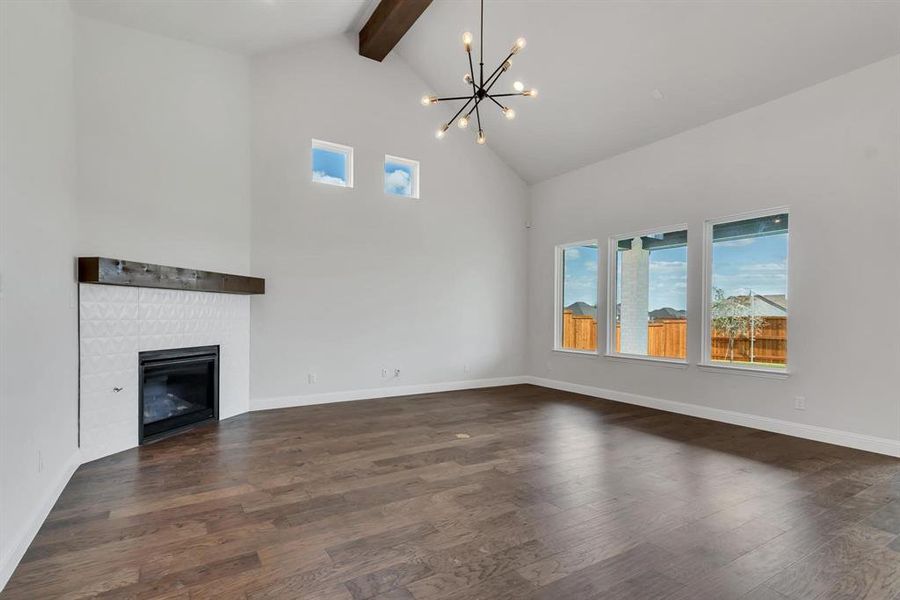 Unfurnished living room featuring beamed ceiling, a fireplace, dark hardwood / wood-style floors, high vaulted ceiling, and a chandelier