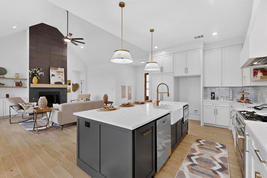 Kitchen featuring white cabinetry, stainless steel appliances, a large fireplace, custom range hood, and an island with sink