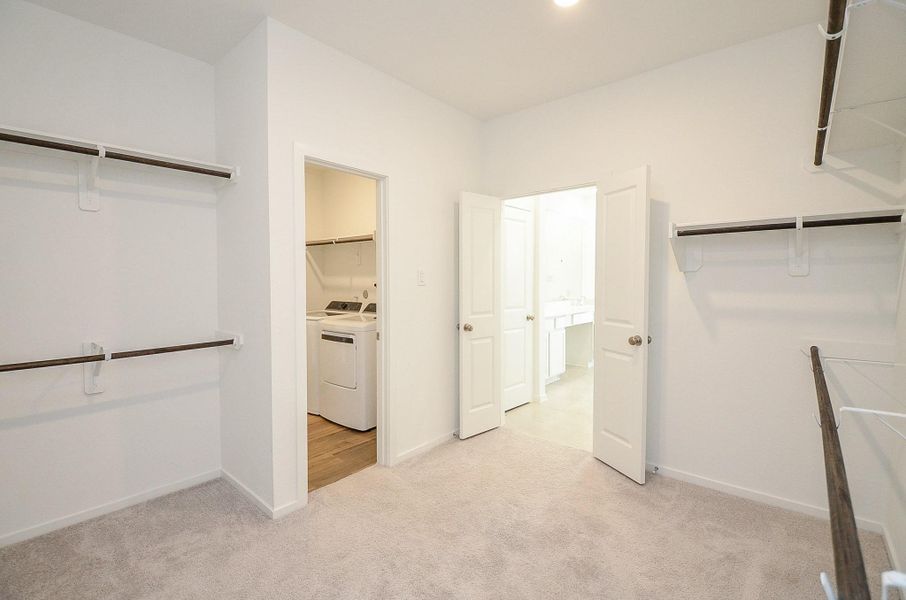 Another view of the primary closet showing entry to the laundry room and en suite primary bathroom