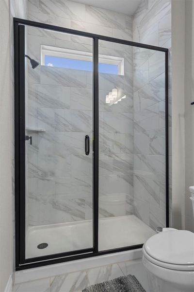 Floor-to-ceiling marble-patterned tile surrounds a modern walk-in shower enclosed by matte black glass framing.