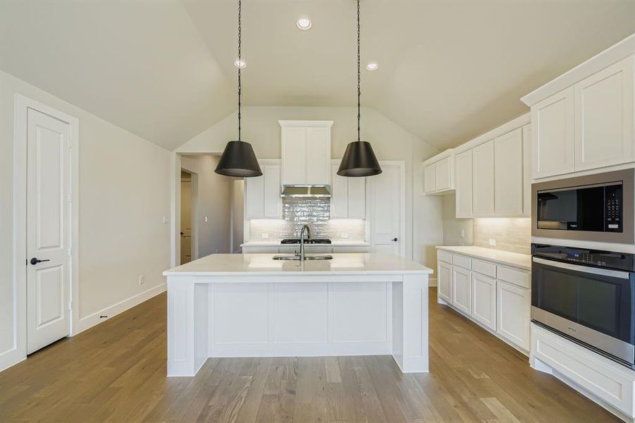 Kitchen with tasteful backsplash, appliances with stainless steel finishes, white cabinets, light wood-type flooring, and lofted ceiling Kitchen with tasteful backsplash, appliances with stainless steel finishes, white cabinets, light wood-type flooring, and lofted ceiling