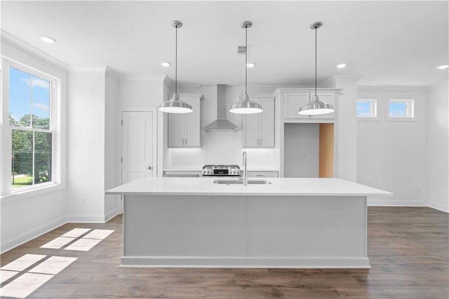 Kitchen featuring ornamental molding, dark wood finished floors, decorative light fixtures, wall chimney exhaust hood, and a center island with sink Kitchen featuring ornamental molding, dark wood finished floors, decorative light fixtures, wall chimney exhaust hood, and a center island with sink