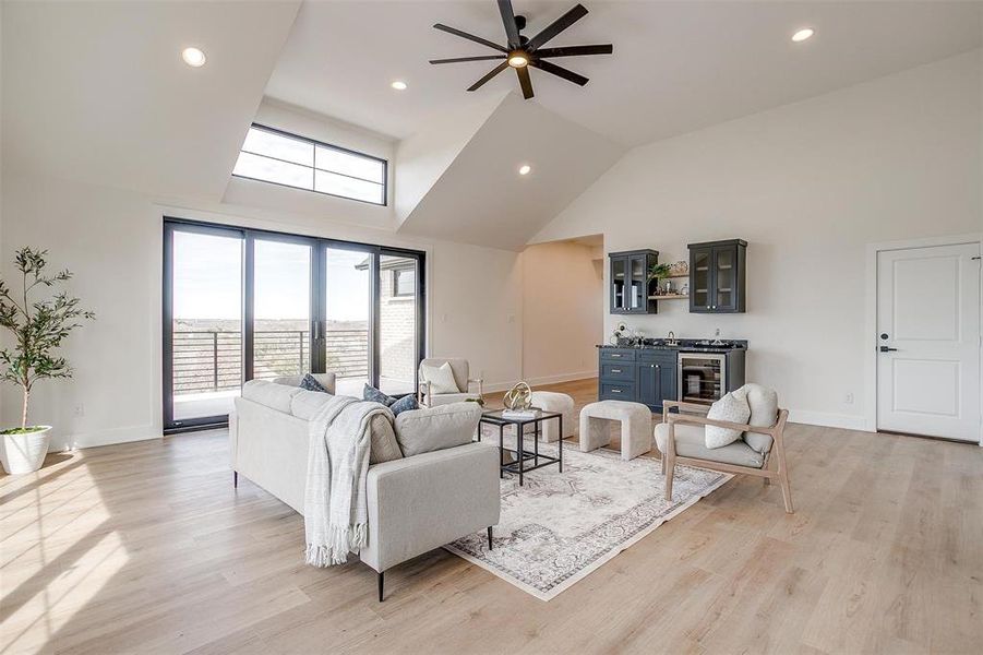 Living area featuring indoor wet bar, baseboards, high vaulted ceiling, and light wood-style flooring