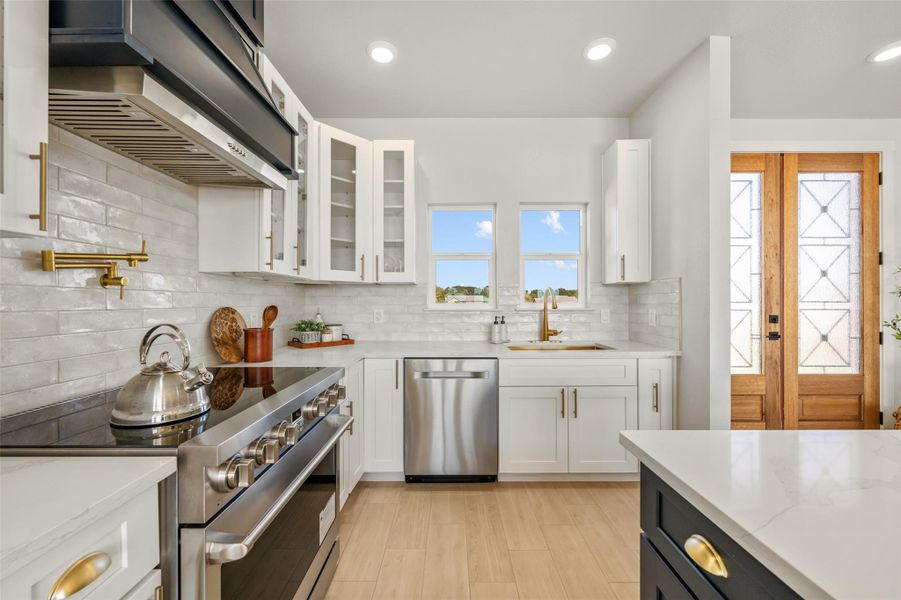 Kitchen featuring white cabinetry, stainless steel appliances, tasteful backsplash, light stone counters, and extractor fan