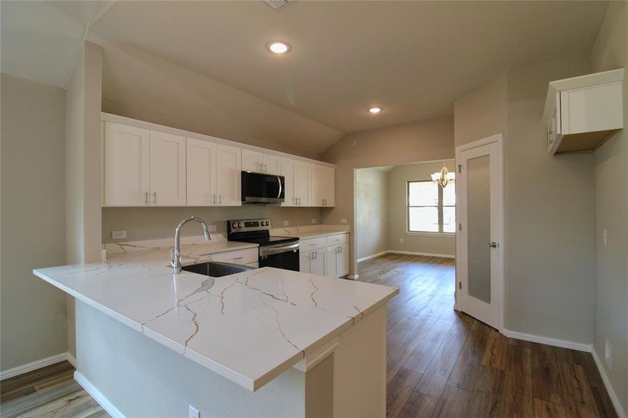 Kitchen featuring a peninsula, white cabinets, appliances with stainless steel finishes, dark wood-type flooring, and a chandelier