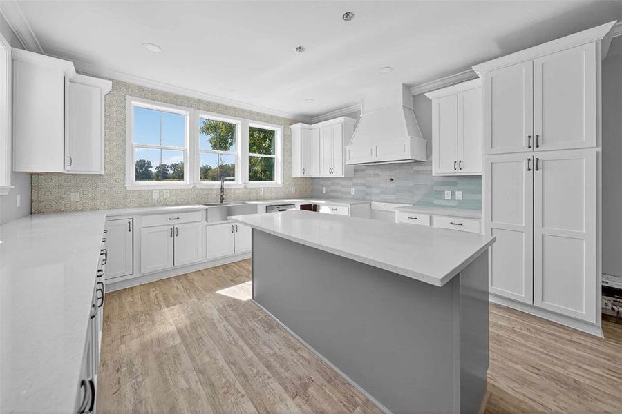 Kitchen with decorative backsplash, white cabinetry, custom exhaust hood, light stone counters, and light wood-type flooring