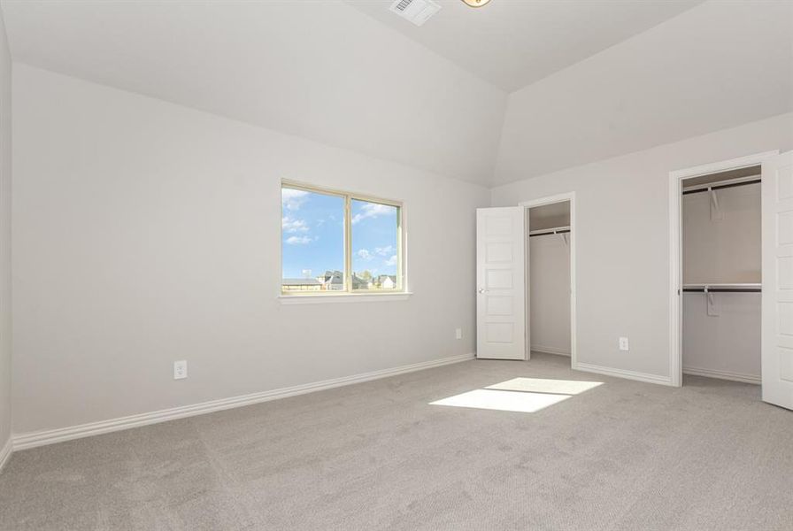 Unfurnished bedroom featuring multiple closets, light carpet, and vaulted ceiling