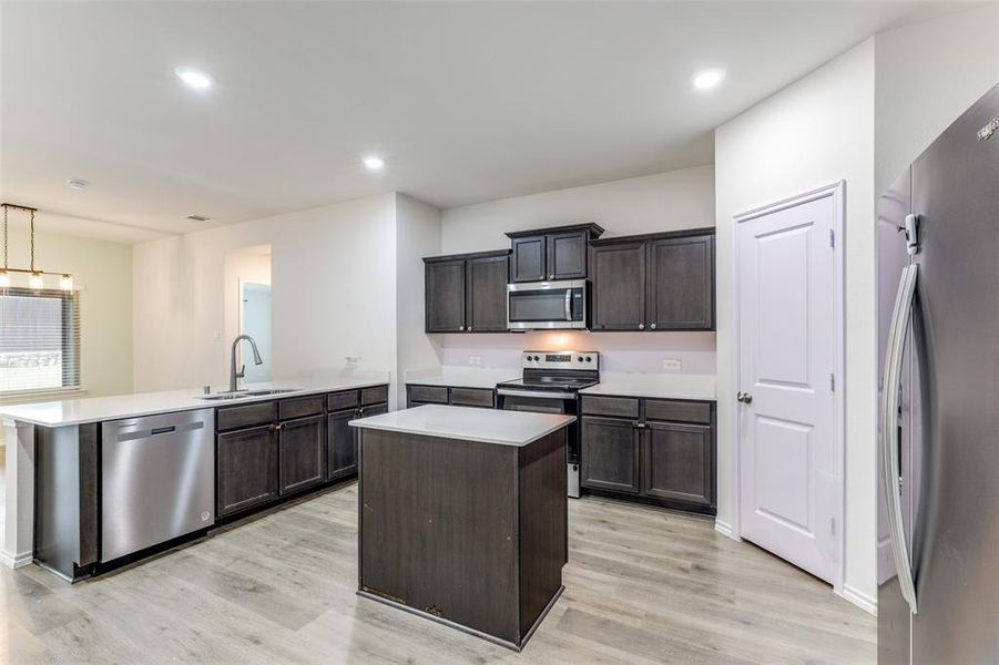Modern kitchen featuring dark wood cabinetry, white countertops, a central island, stainless steel appliances, and wood-finish flooring Modern kitchen featuring dark wood cabinetry, white countertops, a central island, stainless steel appliances, and wood-finish flooring
