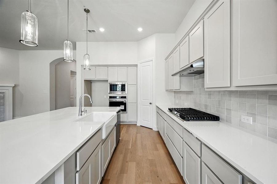 Kitchen featuring pendant lighting, light wood-style flooring, light stone countertops, tasteful backsplash, and recessed lighting Kitchen featuring pendant lighting, light wood-style flooring, light stone countertops, tasteful backsplash, and recessed lighting