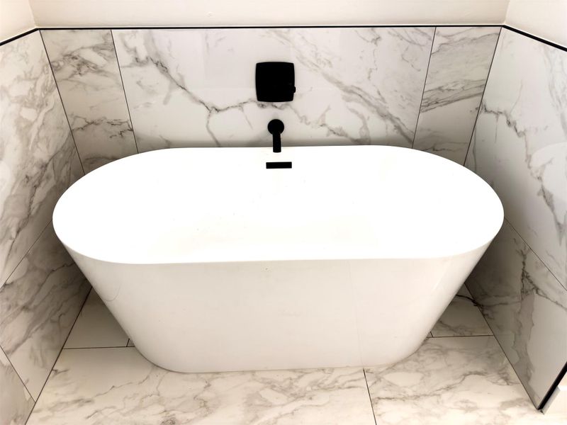An elegant freestanding soaking tub rests against marble-patterned tile walls and matching floors. An elegant freestanding soaking tub rests against marble-patterned tile walls and matching floors.