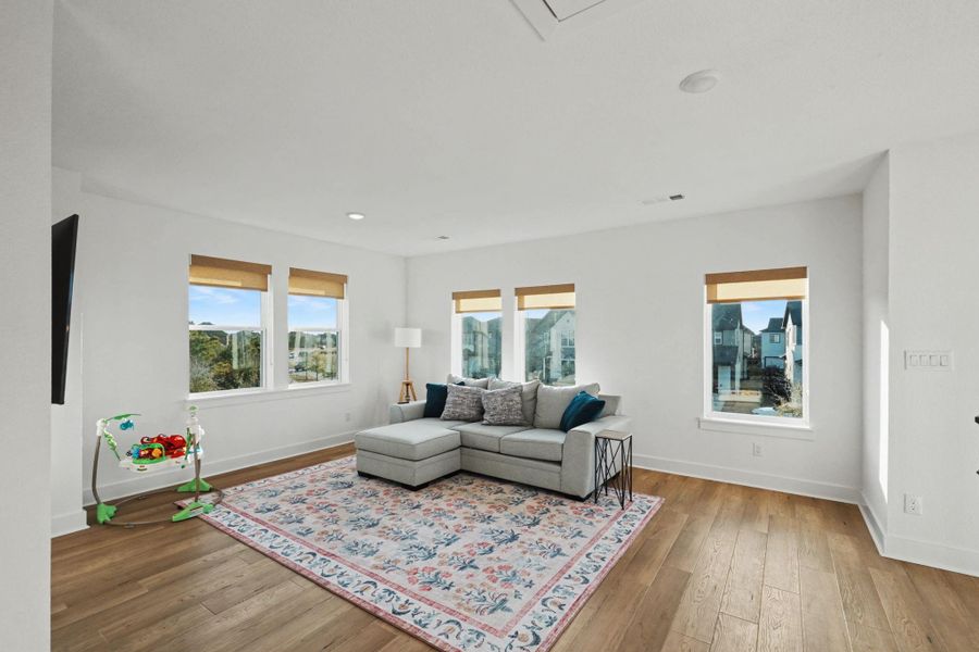 Expansive upstairs living area surrounded by windows, offering beautiful natural light and elevated neighborhood views. With generous floor space and warm wood flooring, this flexible room is ideal for a media lounge, playroom, or second living space.
