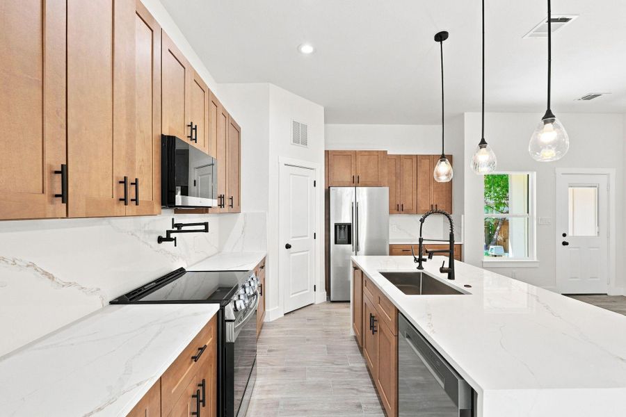 Expansive waterfall quartz kitchen island with an undermount sink and a sleek matte black gooseneck faucet.