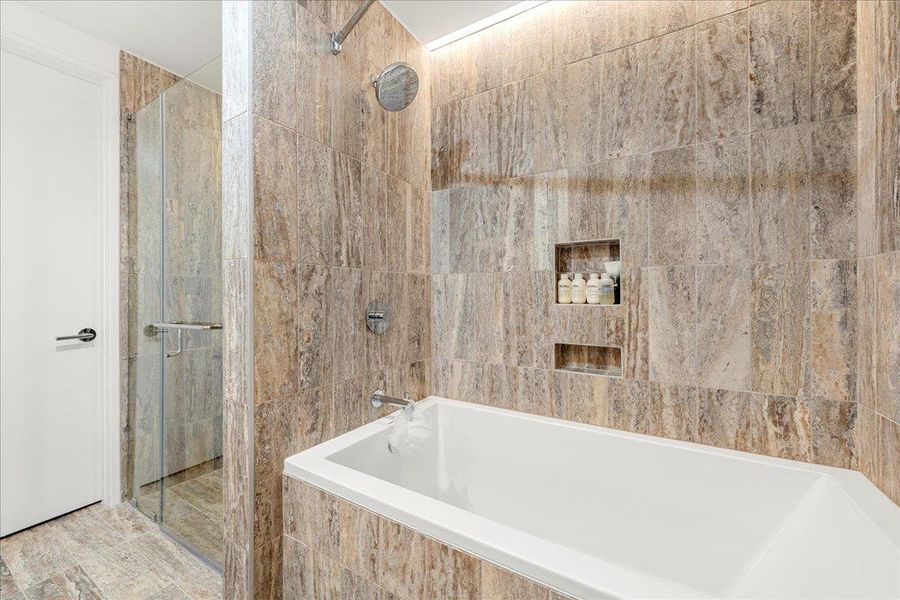Spa-like primary bath with a deep soaking tub and separate walk-in shower wrapped in floor-to-ceiling stone tile. Spa-like primary bath with a deep soaking tub and separate walk-in shower wrapped in floor-to-ceiling stone tile.