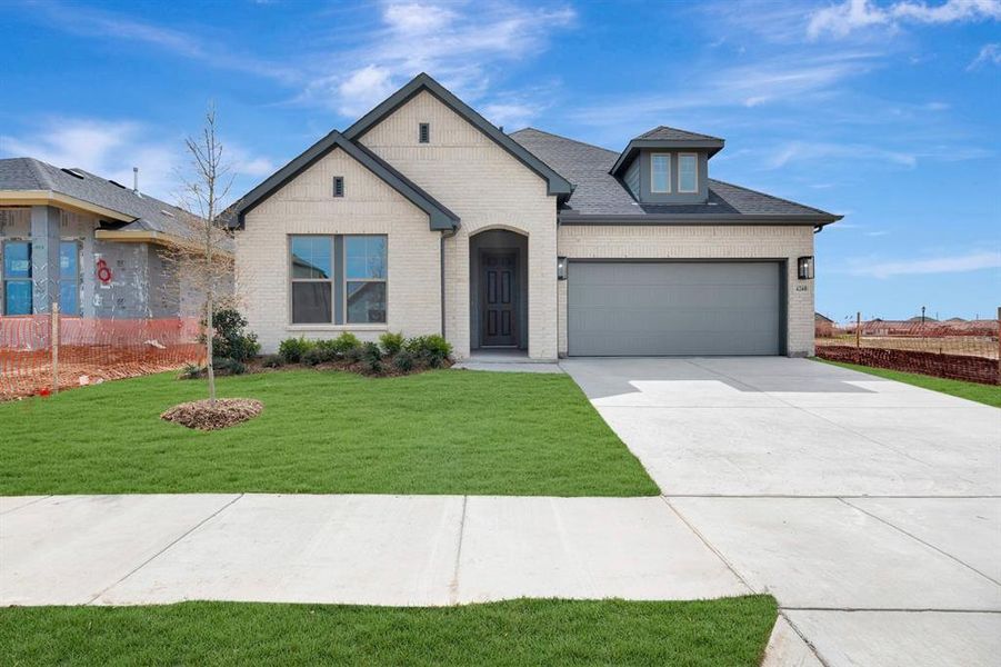 French country home featuring a front lawn, driveway, brick siding, and a garage French country home featuring a front lawn, driveway, brick siding, and a garage