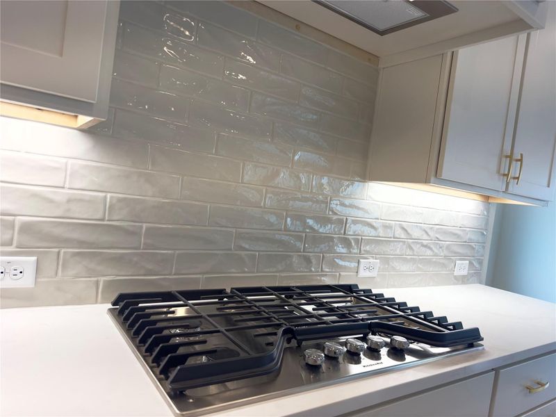Kitchen view of stainless steel gas stovetop, backsplash, and light stone counters