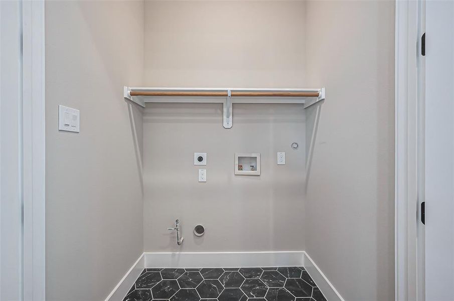 This laundry area boasts stylish black hexagonal tile flooring, washer and dryer hookups, and a convenient overhead storage shelf. The space is enhanced by light, neutral walls.