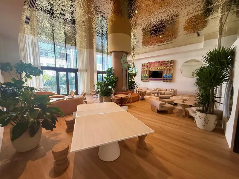 Expansive common area featuring a polished metallic ceiling, wood-finish flooring, floor-to-ceiling windows, and a central structural column