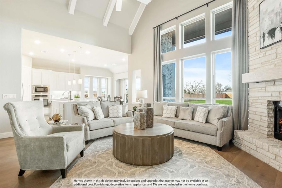 Open-concept living room with vaulted beamed ceiling, stone fireplace, and large windows overlooking backyard