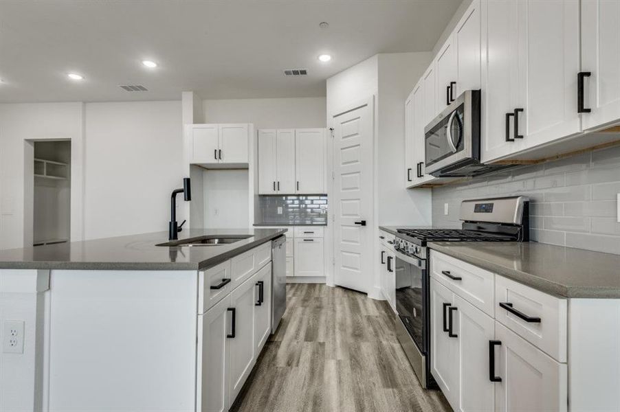 Kitchen featuring stainless steel appliances, sink, a center island with sink, white cabinets, and light hardwood / wood-style floors