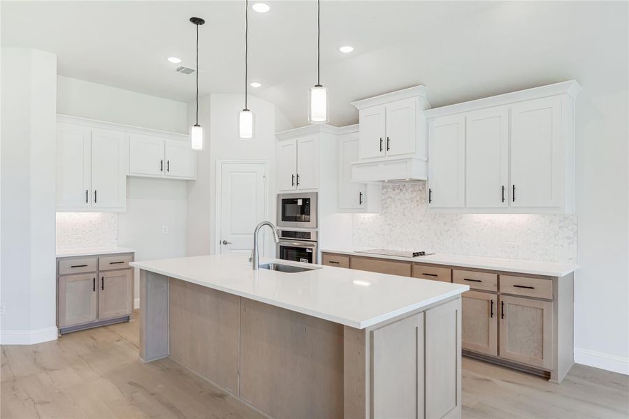 Kitchen with large center island, white upper cabinets, light wood lower cabinets, and stainless steel wall ovens