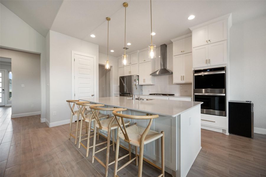 Kitchen featuring a kitchen island with sink, wall chimney range hood, white cabinetry, stainless steel appliances, and recessed lighting