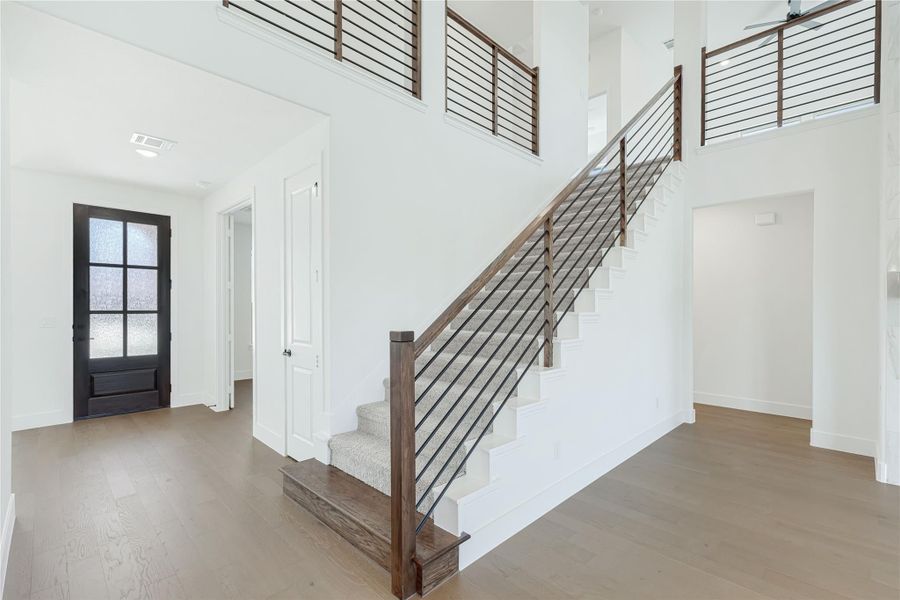 Two-story entryway with wood and metal staircase railing, hardwood floors, and black front door with glass panels