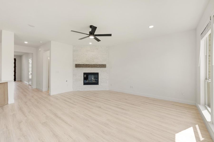 Open living room with light wood floors, stone fireplace, wood mantel, and ceiling fan