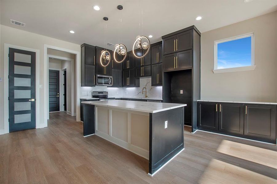 Kitchen featuring a center island, stainless steel appliances, backsplash, decorative light fixtures, and light wood-type flooring