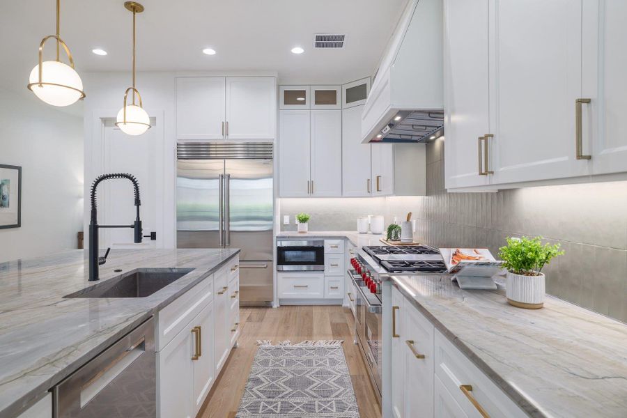 Gourmet kitchen featuring a large island with an undermount sink and matte black faucet, integrated stainless steel appliances, premium countertops, and ample white cabinetry with gold-finish hardware
