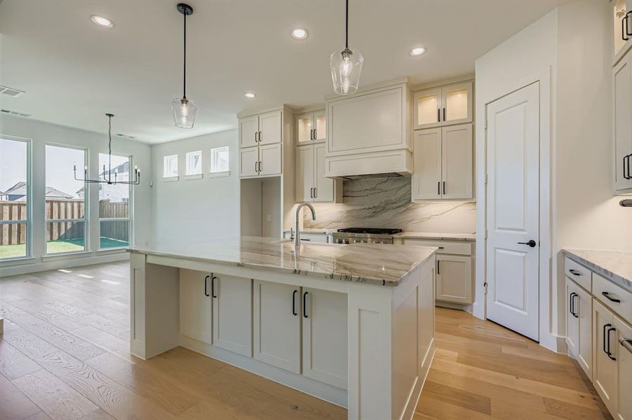 Kitchen featuring light wood-style flooring, light stone countertops, a center island with sink, glass insert cabinets, and recessed lighting