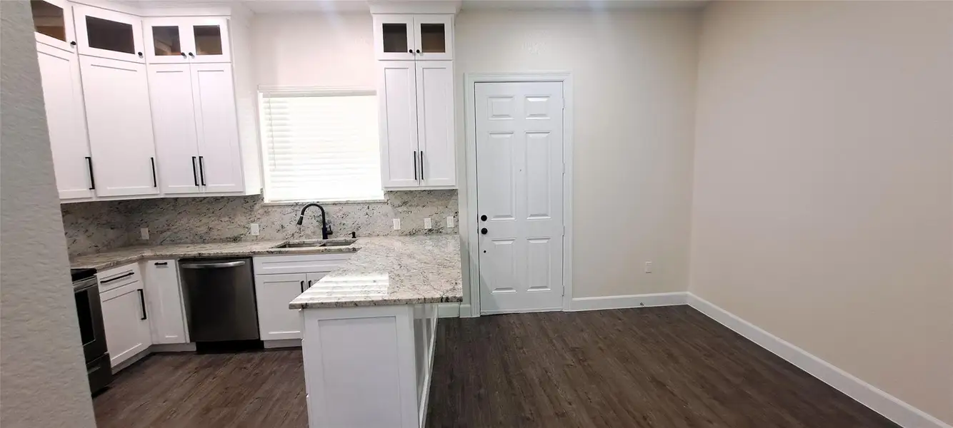Kitchen featuring white cabinets, black stove, dishwasher, light stone countertops, and dark wood-style flooring