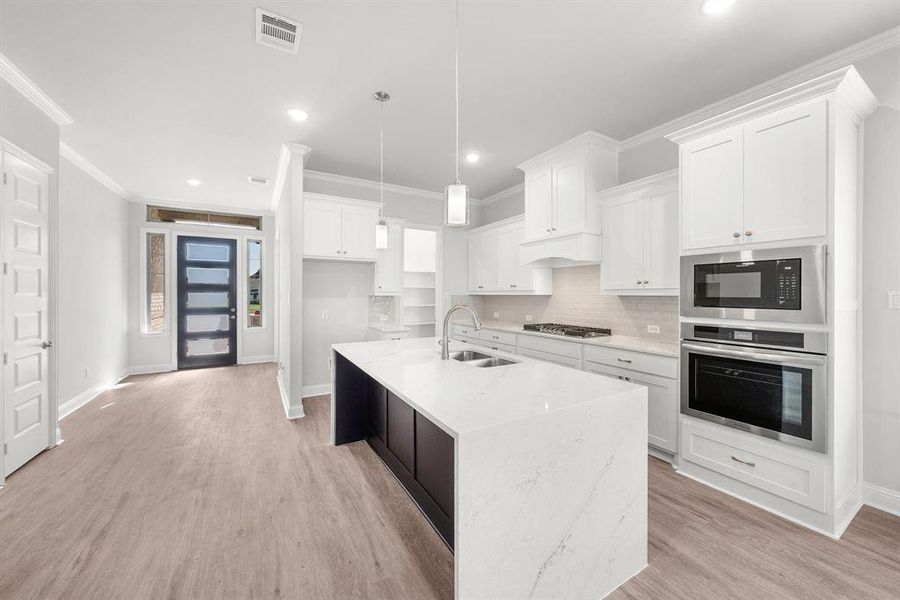 Kitchen with appliances with stainless steel finishes, ornamental molding, recessed lighting, white cabinetry, and a center island with sink