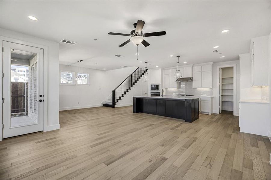 Dual tone kitchen featuring pendant lighting, open floor plan, a kitchen island with sink, decorative backsplash, and a ceiling fan