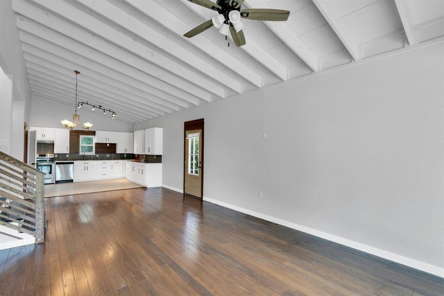 Unfurnished living room featuring a ceiling fan, dark wood-style floors, beamed ceiling, baseboards, and a chandelier
