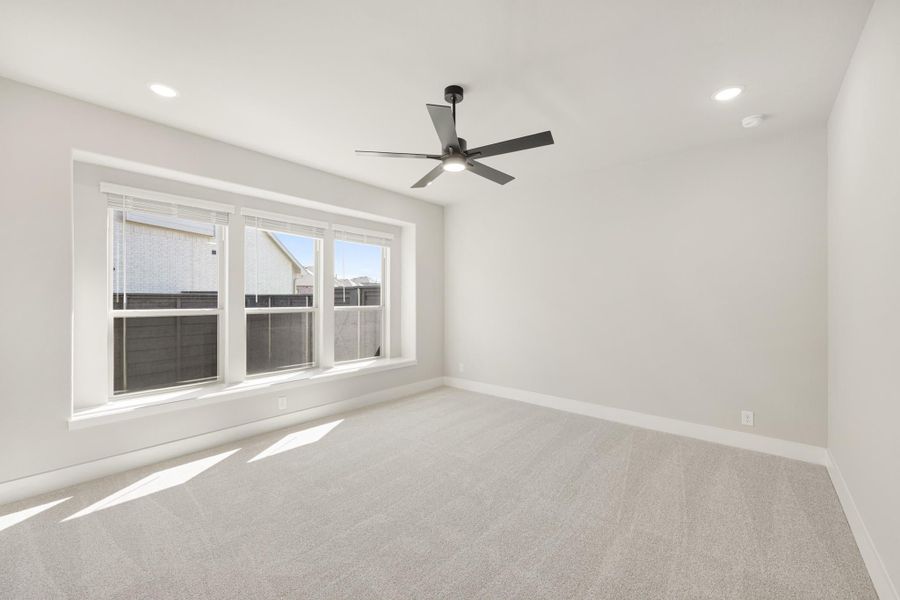 Empty bedroom with light gray carpet, ceiling fan, and triple window with natural light