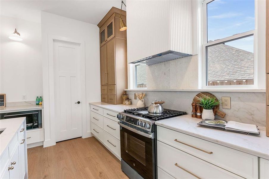 Kitchen featuring stainless steel range with gas stovetop, pendant lighting, extractor fan, light stone countertops, and white cabinetry
