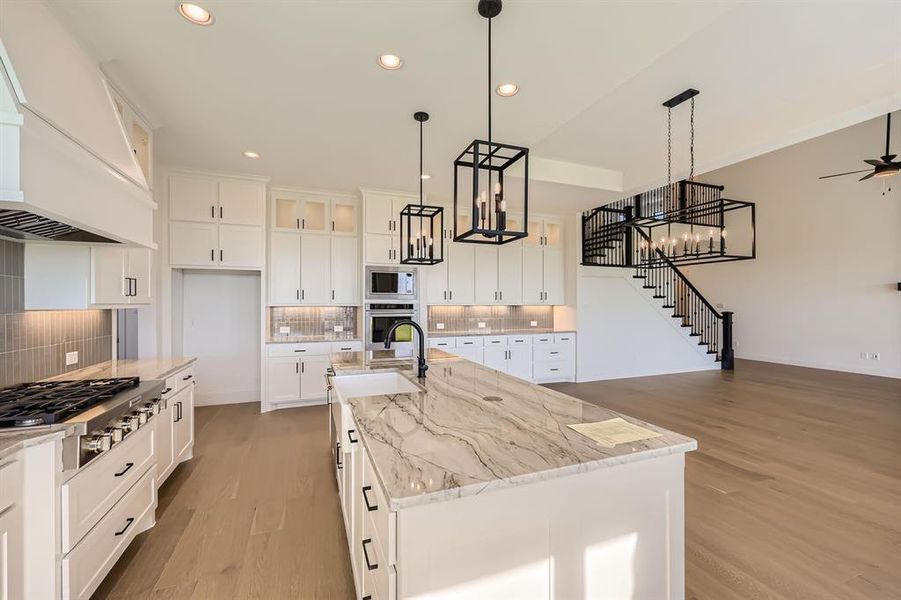 Kitchen featuring stainless steel appliances, hanging light fixtures, a center island with sink, and backsplash