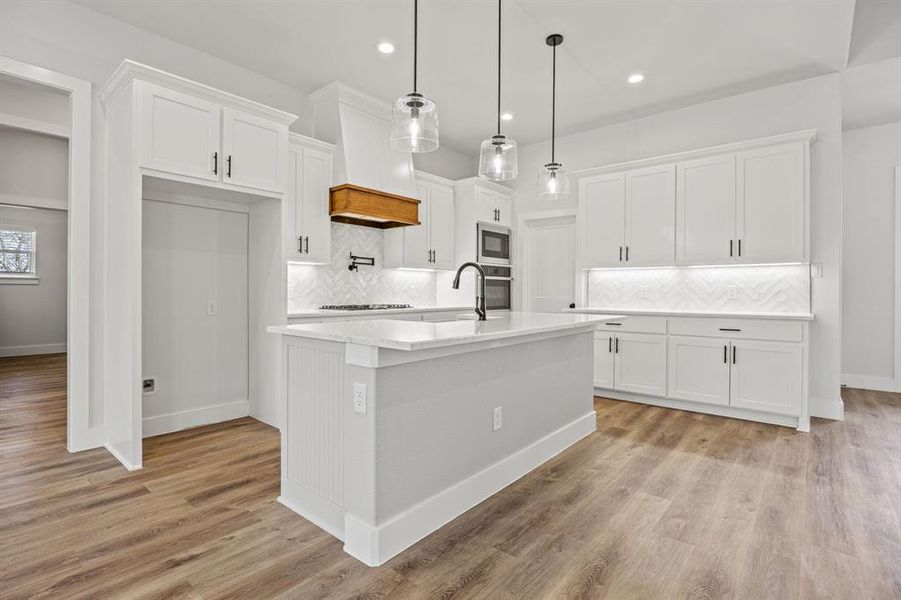 Kitchen featuring white cabinets, light countertops, a kitchen island with sink, hanging light fixtures, and recessed lighting Kitchen featuring white cabinets, light countertops, a kitchen island with sink, hanging light fixtures, and recessed lighting