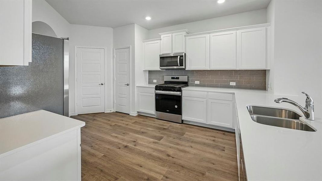 Modern kitchen featuring white cabinetry, light-toned countertops, a stainless steel gas range, and a gray subway tile backsplash