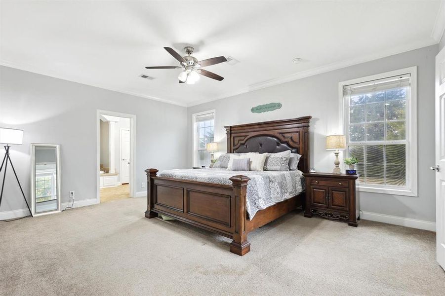 Bedroom featuring multiple windows, ceiling fan, light carpet, and ensuite bath