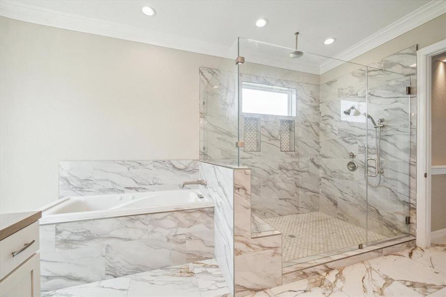 This is a modern bathroom featuring a spacious walk-in shower with a glass enclosure and a separate jacuzzi bathtub, both adorned with marble-style tiles. It includes a built-in tub deck, overhead and hand-held shower fixtures, and is well-lit with recessed lighting.