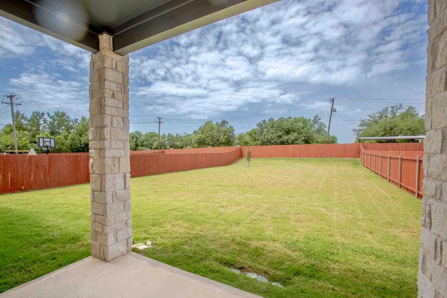 Expansive backyard featuring a manicured lawn, full perimeter privacy fencing, and a concrete patio with stone-clad columns