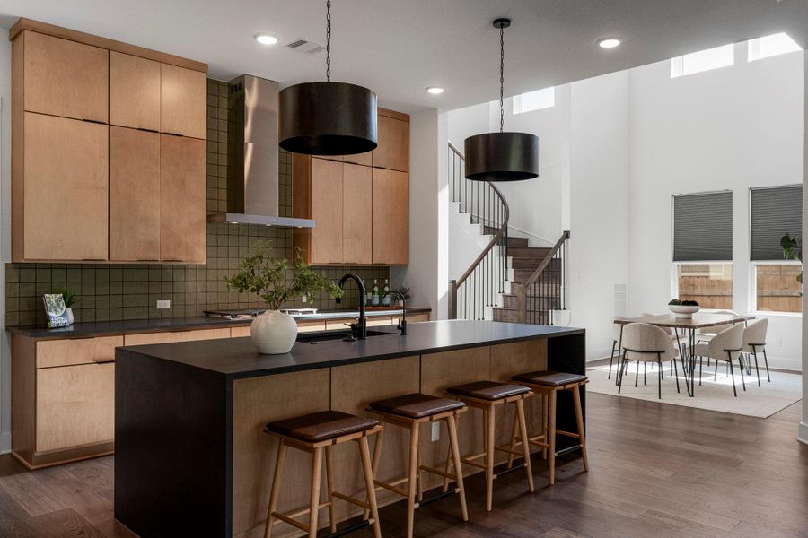 Sleek kitchen with a waterfall island flows into an airy dining space, highlighted by a dramatic curved staircase.