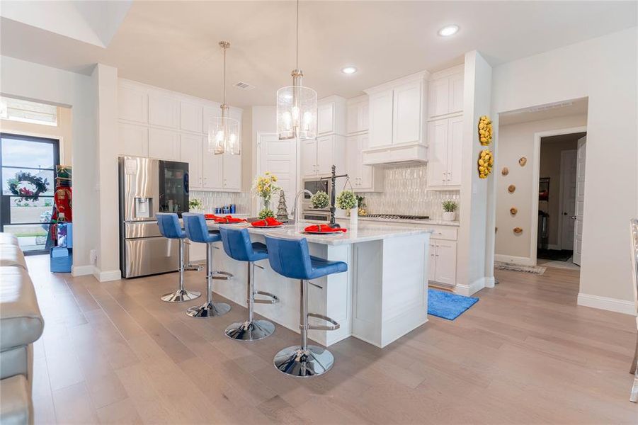 Kitchen with stainless steel fridge with ice dispenser, a kitchen bar, a center island with sink, and white cabinetry