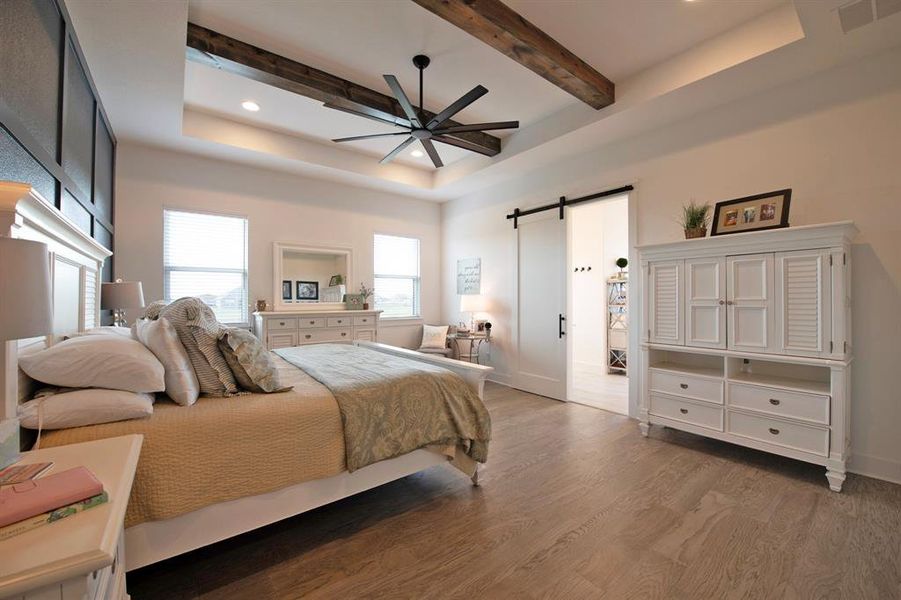 Bedroom featuring a barn door, light wood finished floors, a raised ceiling, a ceiling fan, and recessed lighting