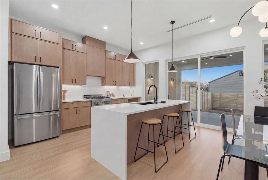 Kitchen featuring freestanding refrigerator, light wood finish cabinetry, a center island with sink, and light wood-style flooring