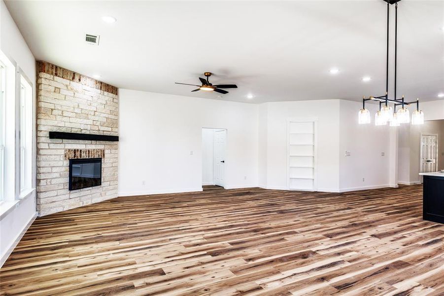 Unfurnished living room featuring wood finished floors, a stone fireplace, recessed lighting, built in shelves, and ceiling fan