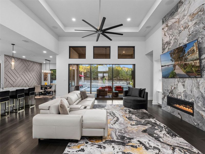Living area featuring a fireplace, dark wood-style floors, an accent wall, ceiling fan, and a high ceiling